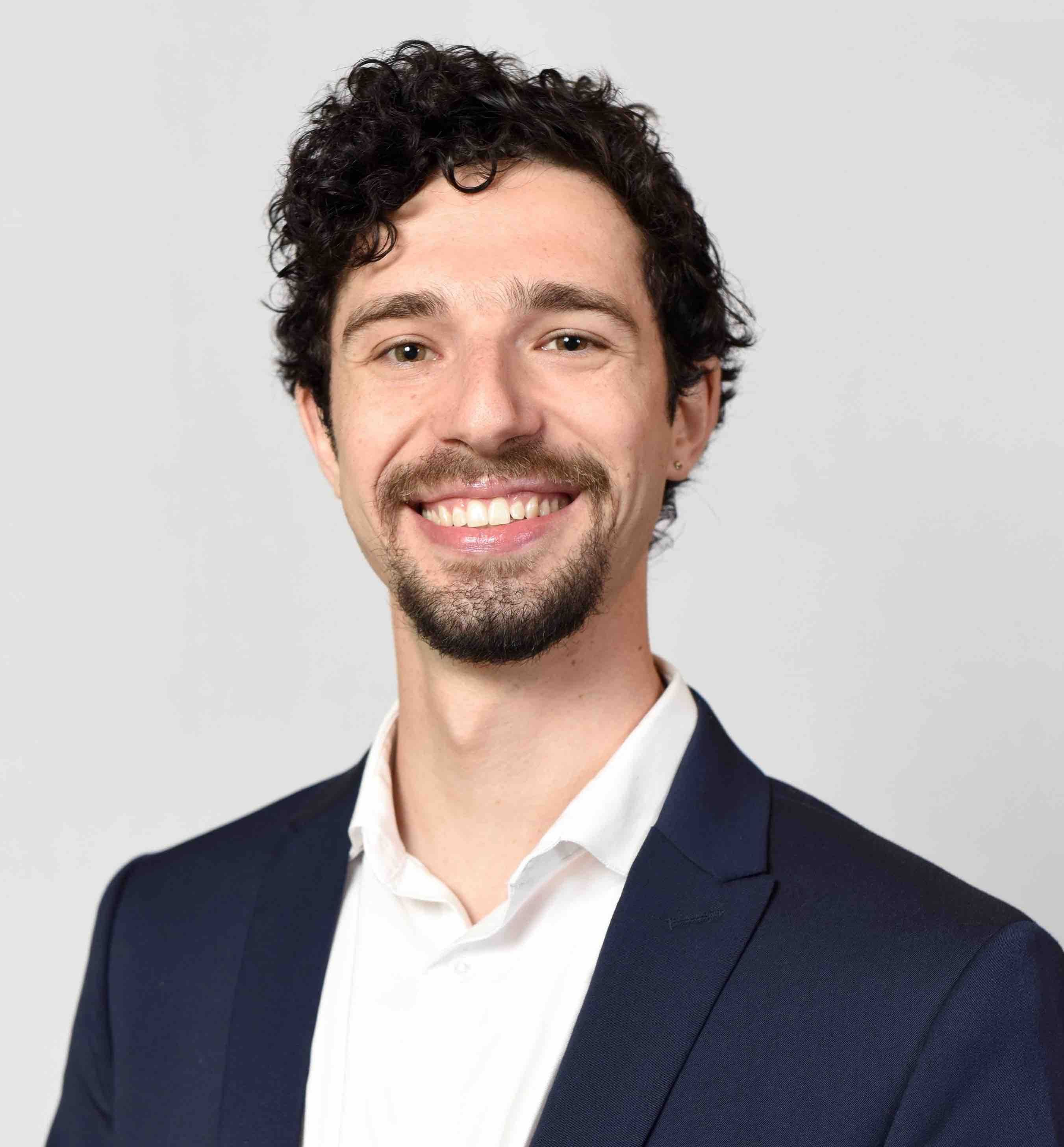 A portrait of Jaron wearing a white dress shirt and navy blue suit coat